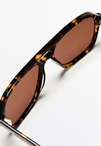 Tortoiseshell sunglasses with brown lenses, featuring a thick frame and sleek temples. The design is angular, showcasing a glossy texture.