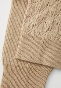 Beige kötött lábszármelegítők bordázott textúrával és gyémánt mintával. Puha anyag, amelyben a varrás és a vastagság váltakozik.