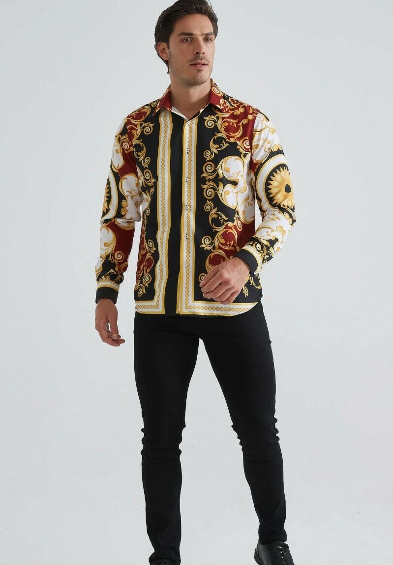 Homme debout portant une chemise à manches longues avec des motifs baroques ornés en rouge, noir, or et blanc, associée à un pantalon et des chaussures noires.