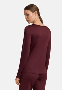 Långärmad vinröd topp i mjukt material, med rundad halsringning och slät yta, matchat med byxor i samma färg.