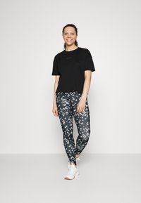 T-shirt preto cropped, leggings pretas com padrão floral e ténis brancos. As leggings apresentam um design floral texturizado em branco e cinza.