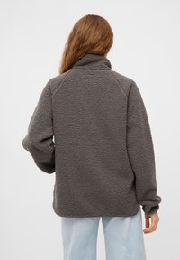 Pullover in pile grigio con superficie texturizzata, colletto alto e maniche raglan. Presenta una vestibilità comoda e cade appena sotto la vita.