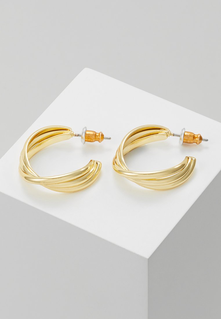 Boucles d'oreilles en métal doré en forme de créoles avec un design torsadé et une finition texturée, maintenues par des fermoirs en argent et en bois.