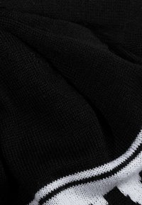 Tessuto nero a maglia con una consistenza morbida, caratterizzato da un design grafico bianco e linee a contrasto lungo il bordo.