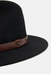 Sombrero de fieltro negro con ala ancha y una banda de cuero marrón que presenta un emblema metálico. Textura suave con un diseño clásico.
