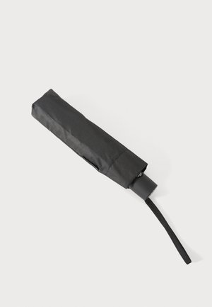 Compacto paraguas negro plegado con correa para la muñeca sobre un fondo claro.