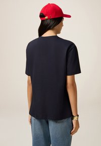 Navyblauw katoenen T-shirt met een rechte snit, korte mouwen en een ronde halslijn. Gemaakt in combinatie met lichtgekleurde denim jeans en een rode pet.