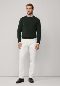 Maglione girocollo verde scuro, pantaloni bianchi e scarpe nere in pelle. Camicia a colletto azzurra visibile sotto il maglione. Design semplice.