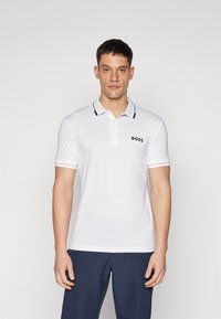 Biely polo tričko s čiernym golierom a akcentmi na rukávoch, so malým čiernym logom na hrudi. Vyrobené z hladkej, priedušnej tkaniny.