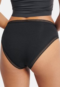 Slip a vita alta in cotone nero con bordo in pizzo smerlato lungo la vita e l'orlo delle gambe, dalla texture liscia e vestibilità aderente.