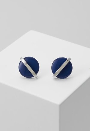Boucles d'oreilles circulaires bleu marine avec une bande diagonale argentée. Finition brillante, montées sur un support blanc. Design minimaliste.