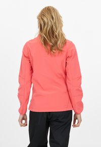 Koraal softshell jack met lange mouwen, aansluitend ontwerp, contrasterende stiksels en minimale hardware. Achteraanzicht, met gestructureerde stof.