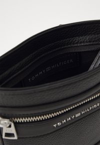 Black leather handbag with textured surface, featuring silver-toned hardware and a zip closure. Interior label reads "TOMMY HILFIGER."