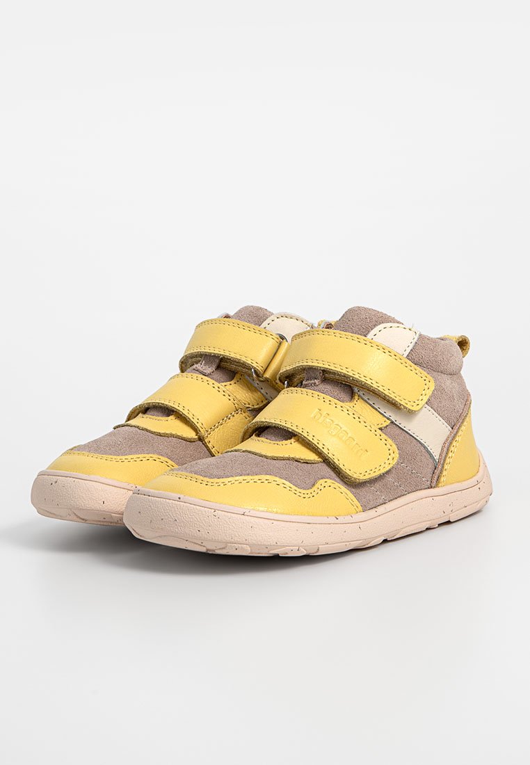 Żółto-brązowe dziecięce sneakersy z dwiema regulowanymi rzepami, gumową podeszwą i fakturowaną powierzchnią. Udekorowane białymi detalami.