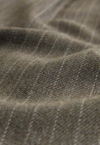 Brun och beige fiskbensmönstrad tyg med en texturerad yta, som har fina vertikala ränder och en mjuk, fallande kvalitet.