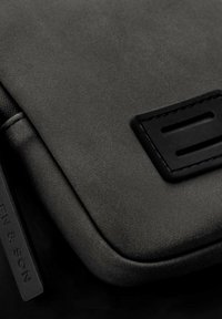 Czarna skórzana torba o gładkiej fakturze, prostych liniach, smukłym kształcie i subtelnym detalem logo na prostokątnym naszywce.