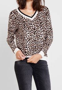 Pull à motif léopard avec manches longues, col en V et poignets côtelés. Le tissu est doux avec un accent blanc et noir au niveau de l'encolure et de l'ourlet.