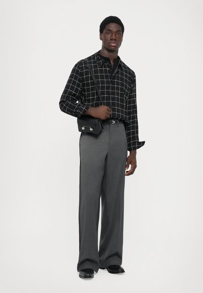 Zwart-wit geruit overhemd met lange mouwen, grijze wijde broek, en een kleine zwarte schoudertas. Glad stoftextuur.