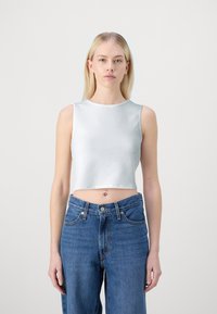 Bílý zkrácený ribbed top vyrobený z texturované tkaniny, kombinovaný s vysokými modrými džíny s knoflíkovým zapínáním a kapsami.