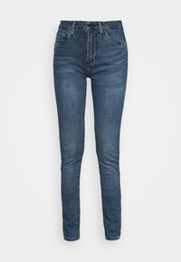 Los jeans skinny en denim azul oscuro, con un diseño de tiro alto, cuentan con bolsillos frontales y cierre con cremallera. Textura suave con ligeros detalles de desgaste.