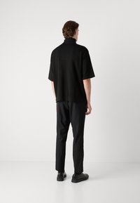 Černý krátký rukávový pulovr s vysokým límcem, kombinovaný s černými kalhotami a černými botami. Látka má hladkou texturu bez viditelných vzorů.