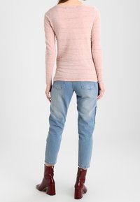 Helles rosa Langarmoberteil mit strukturierten Streifen, kombiniert mit ausgewaschenen blauen Jeans und dunkelroten Stiefeletten mit Blockabsatz.