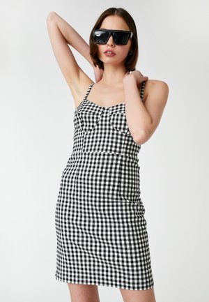 Schwarz-weiß kariertes Kleid mit dünnen Trägern und einer taillierten Silhouette, ausgestattet mit einem quadratischen Ausschnitt und strukturierten Stoffdetails.