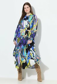 Vestito lungo a camicia con un motivo geometrico blu, verde e nero con illustrazioni di gatti. Include una cintura e maniche lunghe.