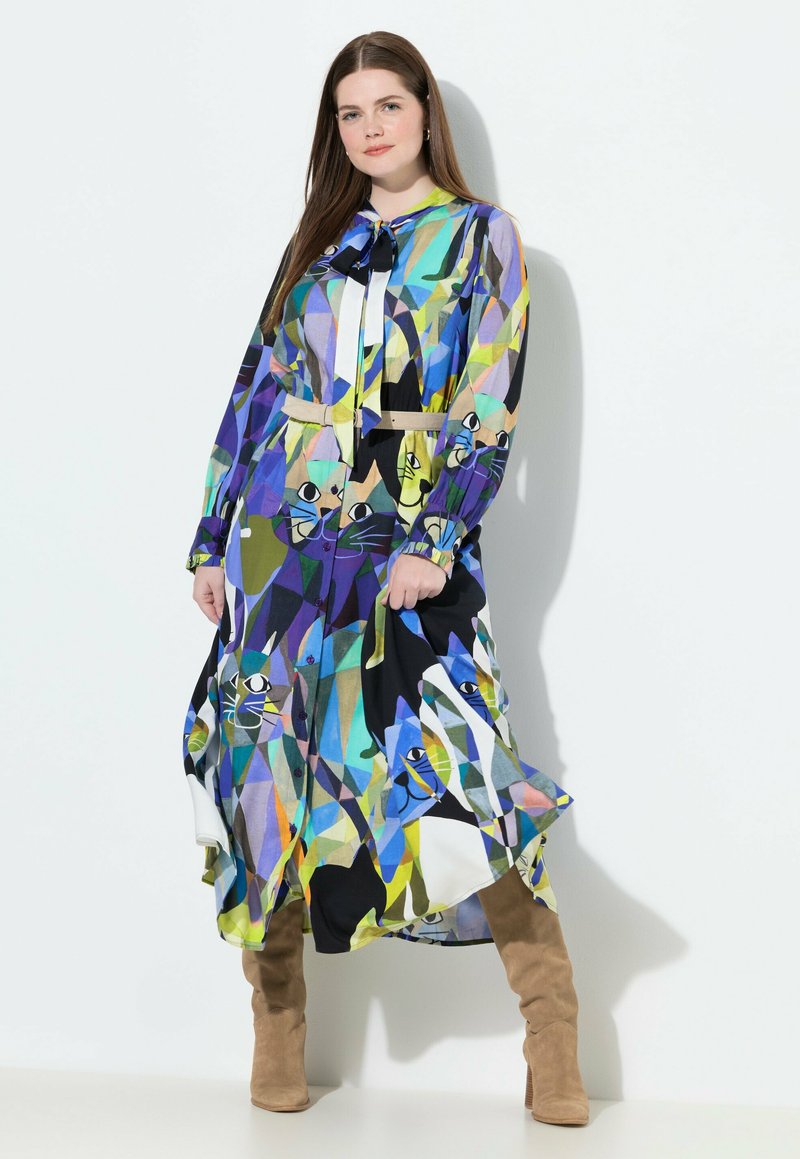 Vestito lungo a camicia con un motivo geometrico blu, verde e nero con illustrazioni di gatti. Include una cintura e maniche lunghe.