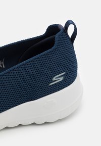 Dunkelblaue Sneaker mit atmungsaktivem Mesh-Obermaterial, elastischem Kragen und weißer Sohle; verfügt über ein silbernes Logo und eine Zuglasche für ein einfaches An- und Ausziehen.