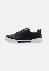 Schwarze Low-Top-Sneaker mit weißer Sohle, goldenen Ösen, strukturiertem Fersenbereich und "Tommy Hilfiger"-Markierung an der Seite.