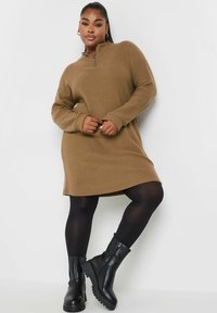Braunes, geripptes Strickkleid mit hohem Kragen und Viertelreißverschluss, kombiniert mit schwarzen Ankle-Boots und schwarzen Strumpfhosen.