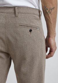 Ruskeat teksturoidut housut, joissa on takatasku mustalla napilla ja koristeommelluksilla, slim fit -muotoilu ja vyölenkit.