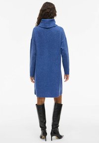 Blå stickad klänning med hög krage, långt ärm och ribbade detaljer vid fållarna. Bärs med svarta knä höga stilettboots.