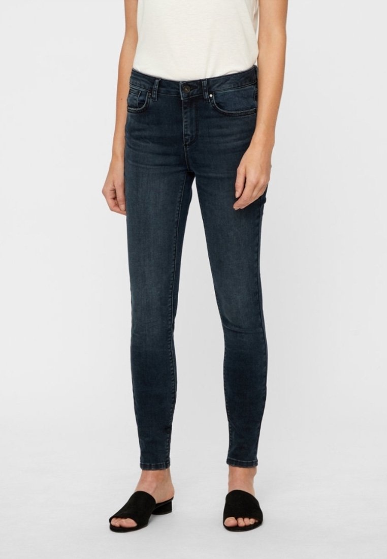 Jeans ajustados de color azul oscuro, fabricados en denim, con un diseño clásico de cinco bolsillos, cierre frontal con cremallera y detalles de costura mínimos.