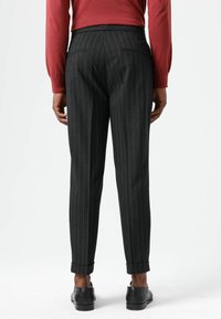 Dunkelgraue Nadelstreifenhose mit schmaler Passform, glatter Textur, Gesäßtaschen und umgeschlagenen Säumen, kombiniert mit schwarzen Schuhen.