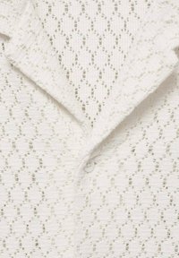 Camisa blanca de punto con un patrón texturizado de formas de rombo, un cuello tipo solapa y un cierre de botones.
