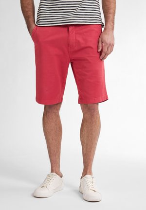 Shorts en coton rouge avec un devant plat, des poches latérales et une coupe droite, associés à des baskets blanches et une chemise rayée.