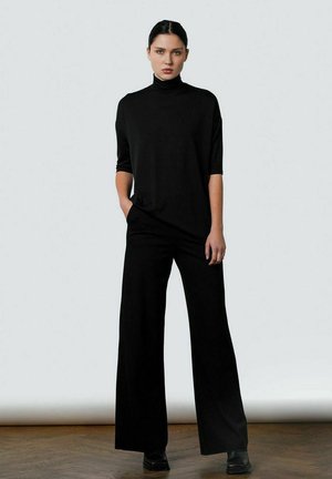 Black turtleneck top with short sleeves and loose-fitting black trousers, made of soft fabric, paired with black ankle boots.