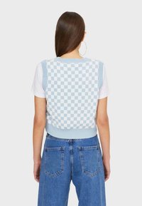 Chaleco de cuadros azul de punto con dobladillo y sisas acanalados, llevado sobre una camiseta blanca, combinado con unos vaqueros azul de cintura alta.