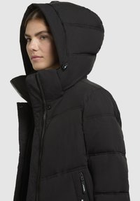 Schwarze Steppjacke mit großer Kapuze, gestepptem Design, Reißverschluss und Druckknopfverschluss sowie seitlichen Reißverschlusstaschen. Weiches, leichtes Material.