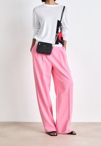 Personne portant un pull blanc avec un imprimé graphique, un pantalon ample rose, des talons noirs à bout ouvert et un sac bandoulière noir à chaîne.