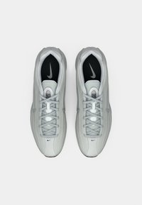 Kerged hallid Nike spordijalanõud, millel on paelad, mustad sisetallad ja nähtavad Nike logod, nähtav ülalt valgel taustal.