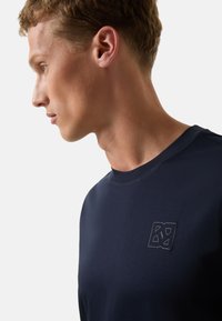 Námořnické modré tričko s kruhovým výstřihem vyrobené z měkké tkaniny, s výrazným embosovaným logem na hrudi a subtilními švy.