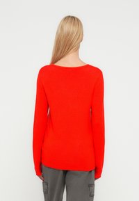 Κόκκινο πλεκτό πουλόβερ με μακριά μανίκια, φαρδύ λαιμόκοψη και ριμπ στη βάση. Το ύφασμα φαίνεται ομαλό με μεσαίο πάχος.