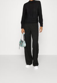 Top lungo a maniche lunghe plissettato nero, pantaloni neri larghi e una borsa iridescente. Le sneakers bianche completano l'outfit.