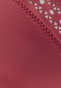 Červená textúrovaná tkanina s hladkým povrchom. Obsahuje vyrezávané geometrické vzory a kontrastné prešité akcenty na okraji.