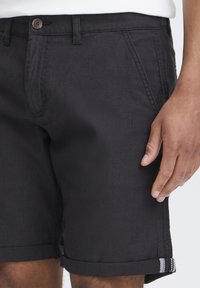 Pantalones cortos negros hechos de una tela ligera, con cierre de botón, bolsillos frontales y dobladillos enrollados con acentos de rayas.