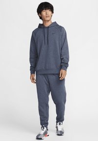 Sudadera con capucha de color azul marino con un bolsillo tipo canguro, combinada con pantalones de chándal a juego. Presenta un logo de Nike en el pecho y zapatillas con un diseño estampado.
