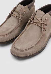 Zapatos de ante beige con una textura suave, diseño de cordones, punta redonda y costuras en contraste; suela de goma para mayor agarre.